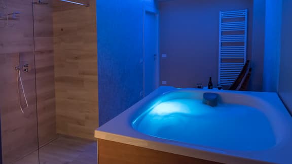 Interno della SPA con vasca idromasaggio e doccia illuminate dalla cromoterapia e dalla luce che esce dalla sauna